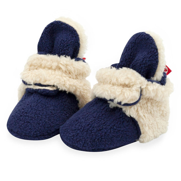 A pair of navy baby booties with beige furry detailing and non-slip gripper soles.