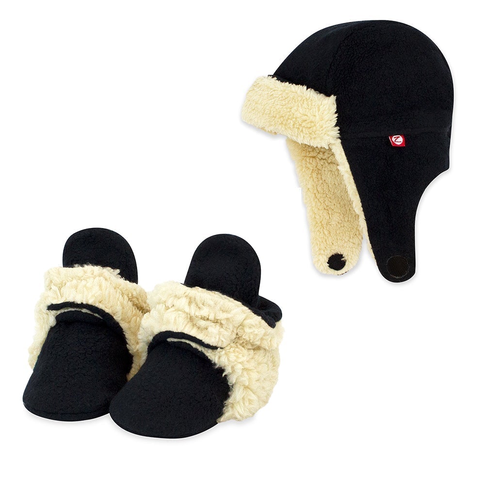 A set of black Cozie Furry Booties and a Trapper Hat for babies, with the hat featuring a beige furry lining visible.