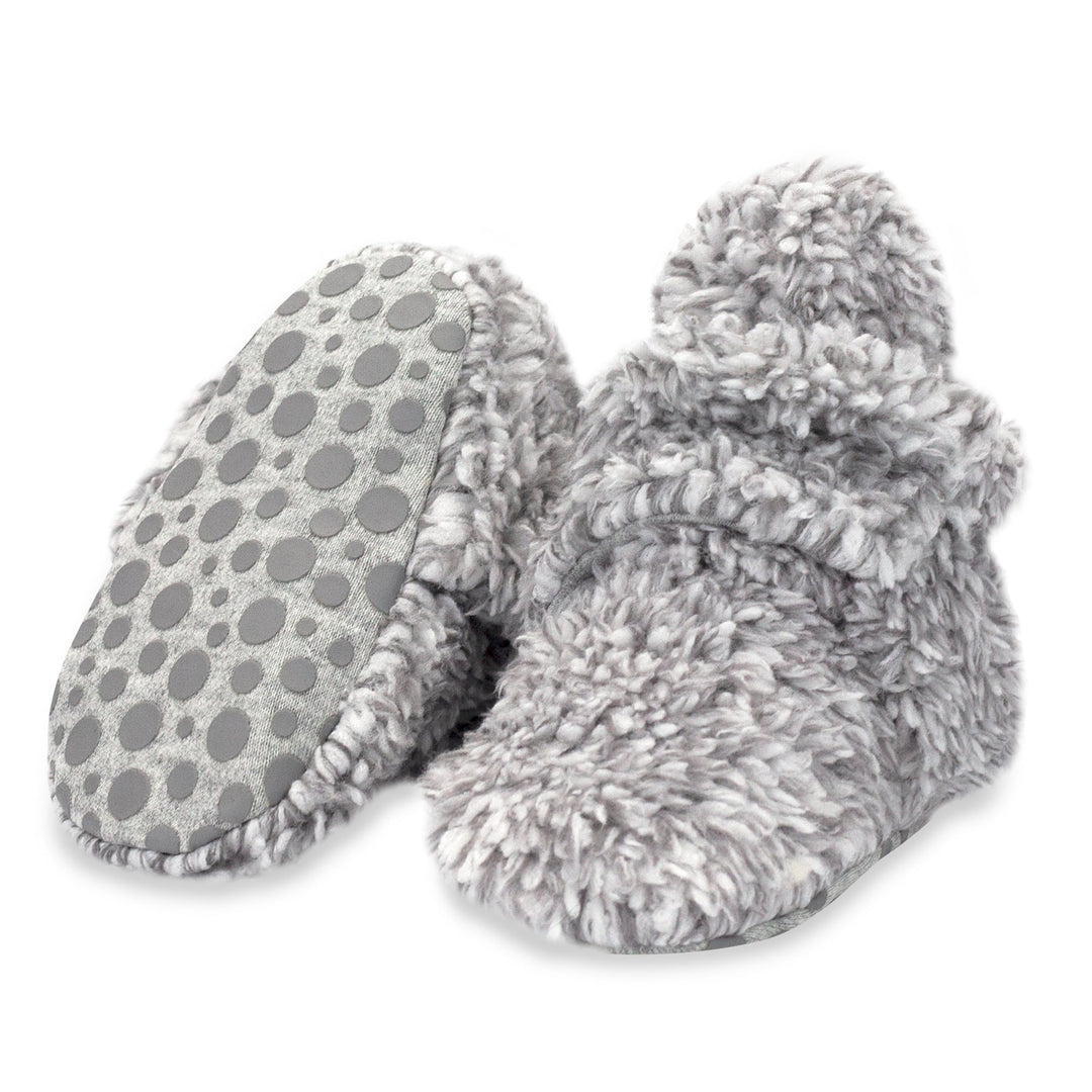 A pair of gray faux fur baby booties with gripper dots on the bottom.