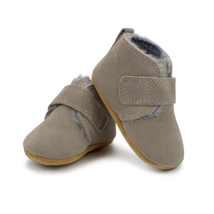 A pair of gray leather baby shoes with furry lining and a Velcro strap across the front.