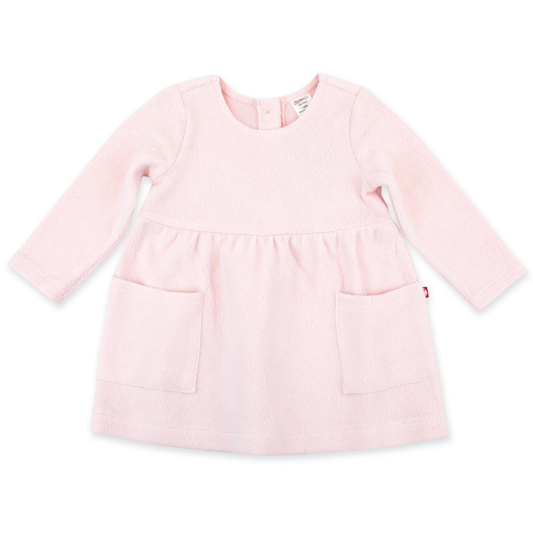 A long-sleeved baby pink fleece dress with two front patch pockets and a button opening at the back.