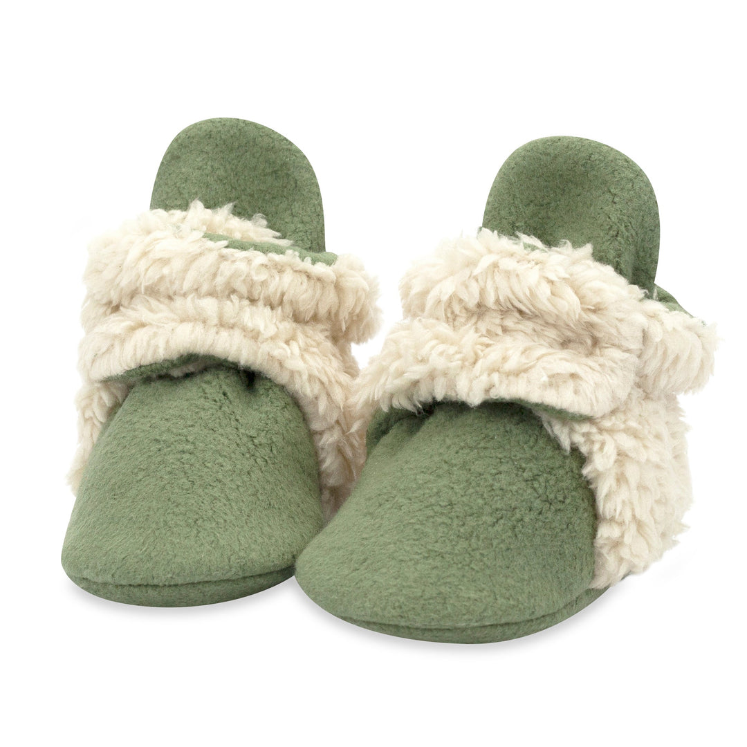 A pair of olive green baby booties with furry white detailing on the heel and strap.