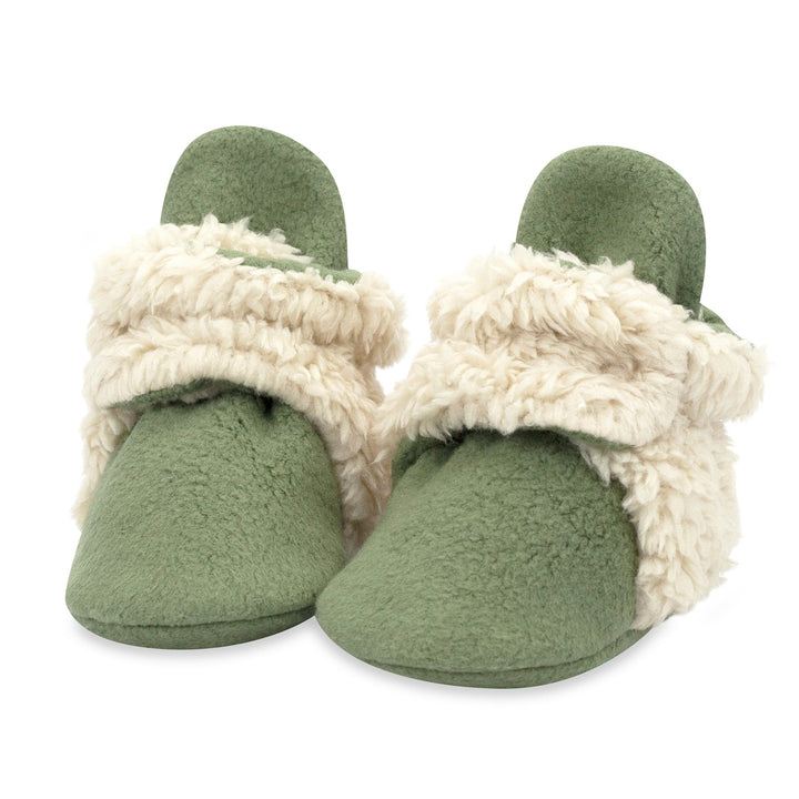 A pair of olive green baby booties with furry white detailing on the heel and strap.