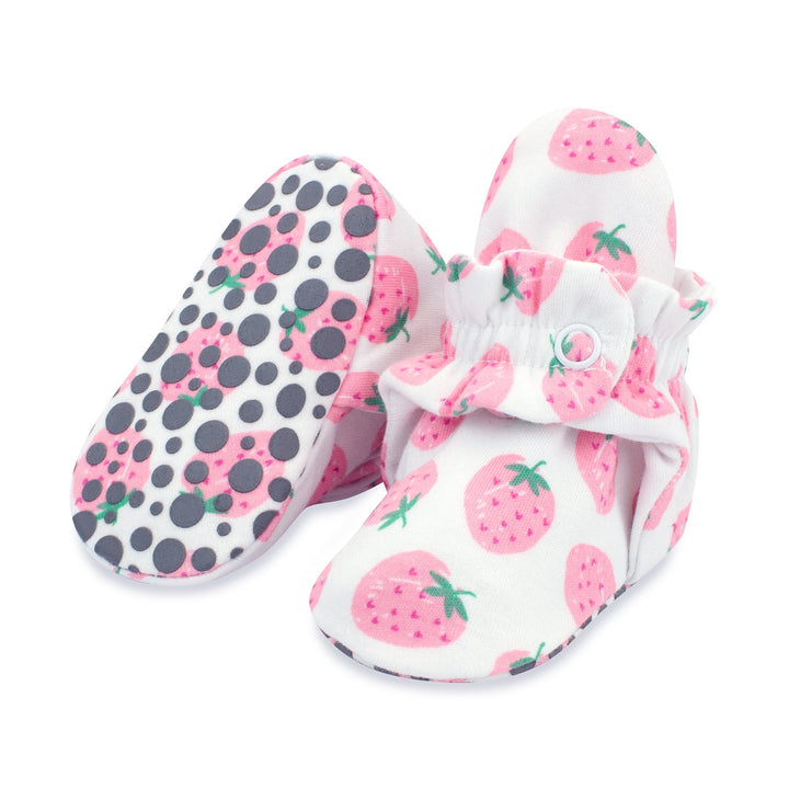 A pair of pink baby booties with a strawberries print and rubber grippers on the sole.