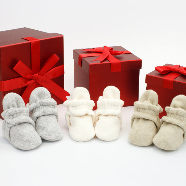 A curated baby gift set featuring Zutano fleece booties, a matching organic cotton hat, and a soft newborn outfit.