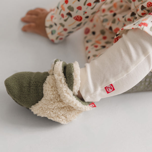 Baby wearing Zutano fleece booties showing the adjustable two-snap closure system and soft-sole construction for foot development