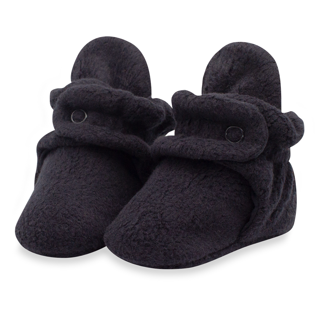 A pair of black fleece baby booties with two adjustable snaps on the top.