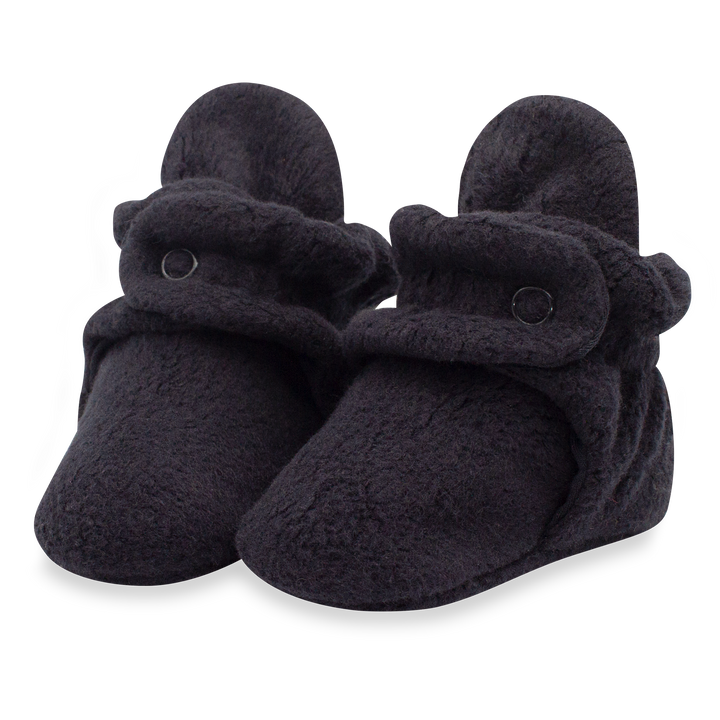 A pair of black fleece baby booties with two adjustable snaps on the top.