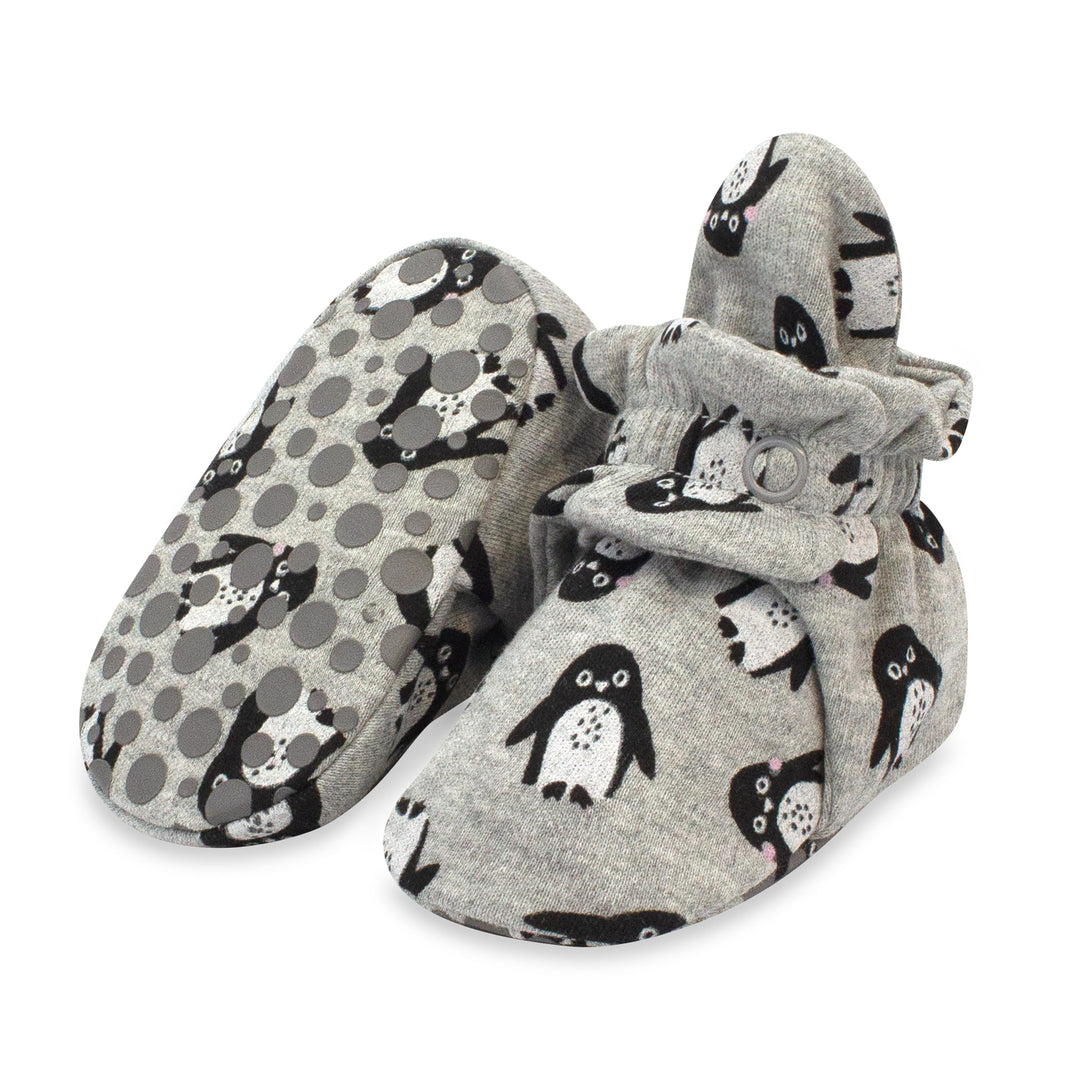 A pair of gray organic cotton baby booties with black penguin prints and a rubber gripper design on the sole.