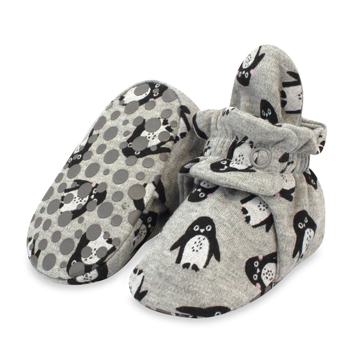 A pair of gray organic cotton baby booties with black penguin prints and a rubber gripper design on the sole.