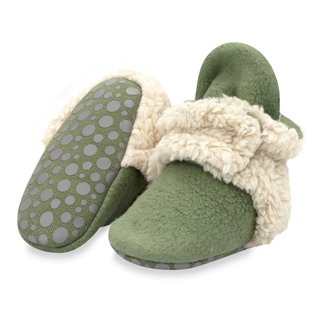 A set of olive green baby booties with furry white detailing on the heel and strap.