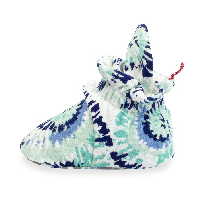 A pair of organic cotton baby booties with a tie-dye pattern in shades of blue and white, featuring rubber grippers on the bottom.
