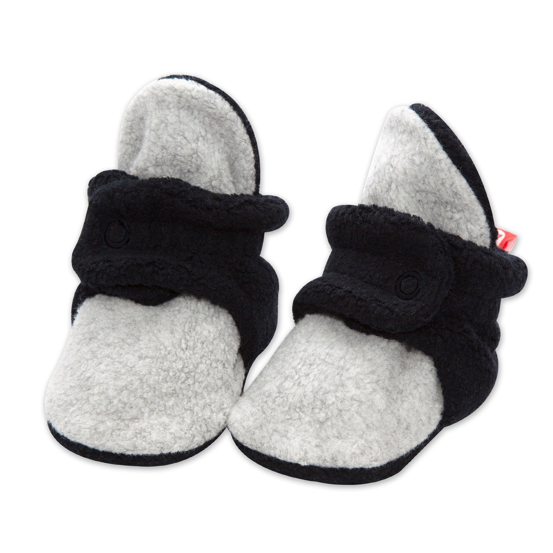 A pair of baby booties with Cozie Fleece lining, in black and heather gray color blocks, featuring non-slip gripper soles and a two-snap design.