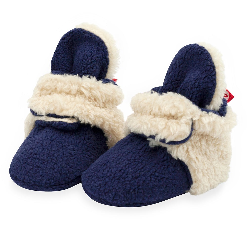 A pair of navy baby booties with beige furry detailing and non-slip gripper soles.