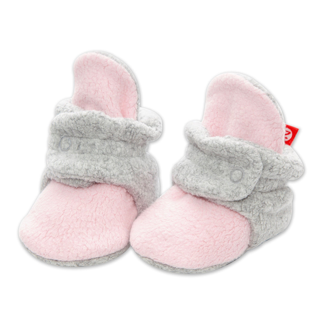 A pair of baby booties in baby pink and heather gray with a fleece lining and two snap closures.