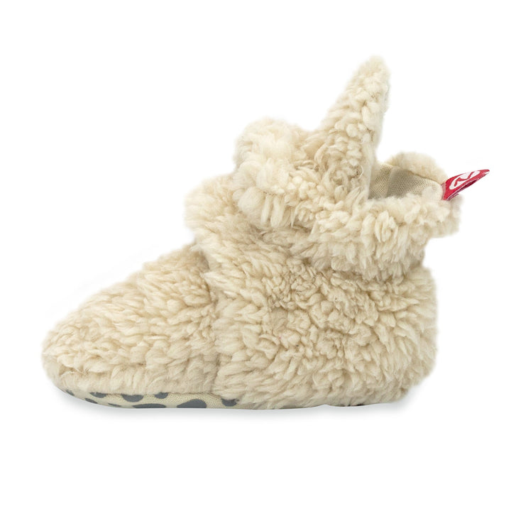 Beige baby booties with faux fur exterior and gripper dots on the sole.