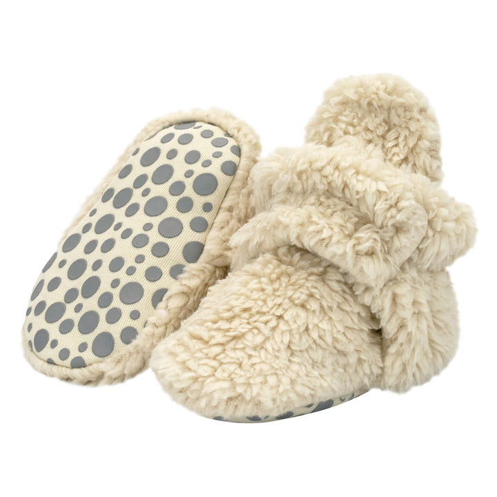 A pair of beige baby booties with faux fur exterior and gripper dots on the sole.