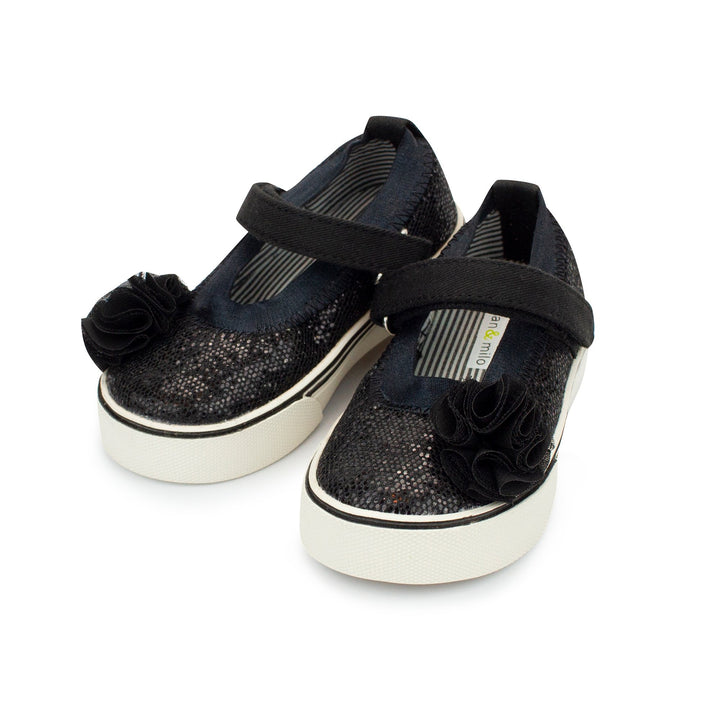 A pair of black glittery Mary Jane shoes with a hook and loop strap and tassel detail.