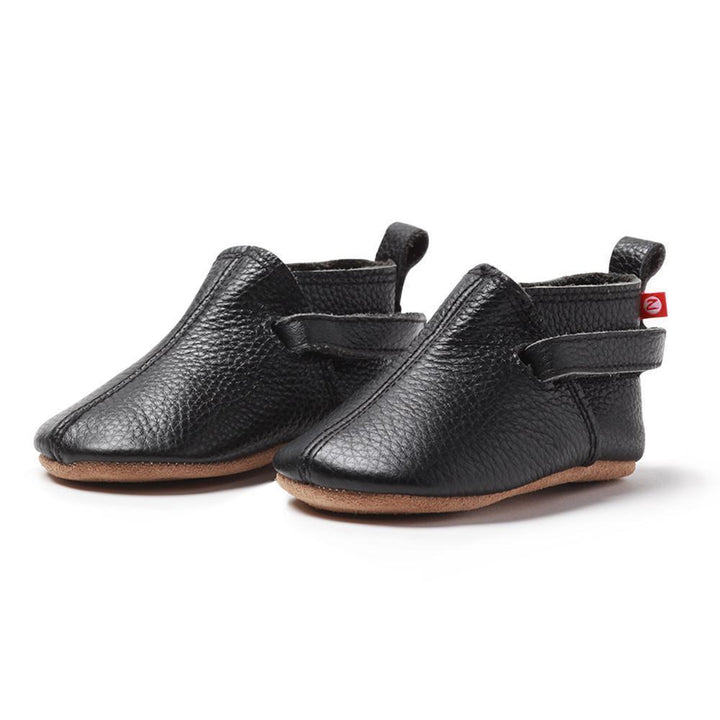 A pair of black leather baby shoes with soft soles, adjustable hook and loop straps, and a cushioned insole.