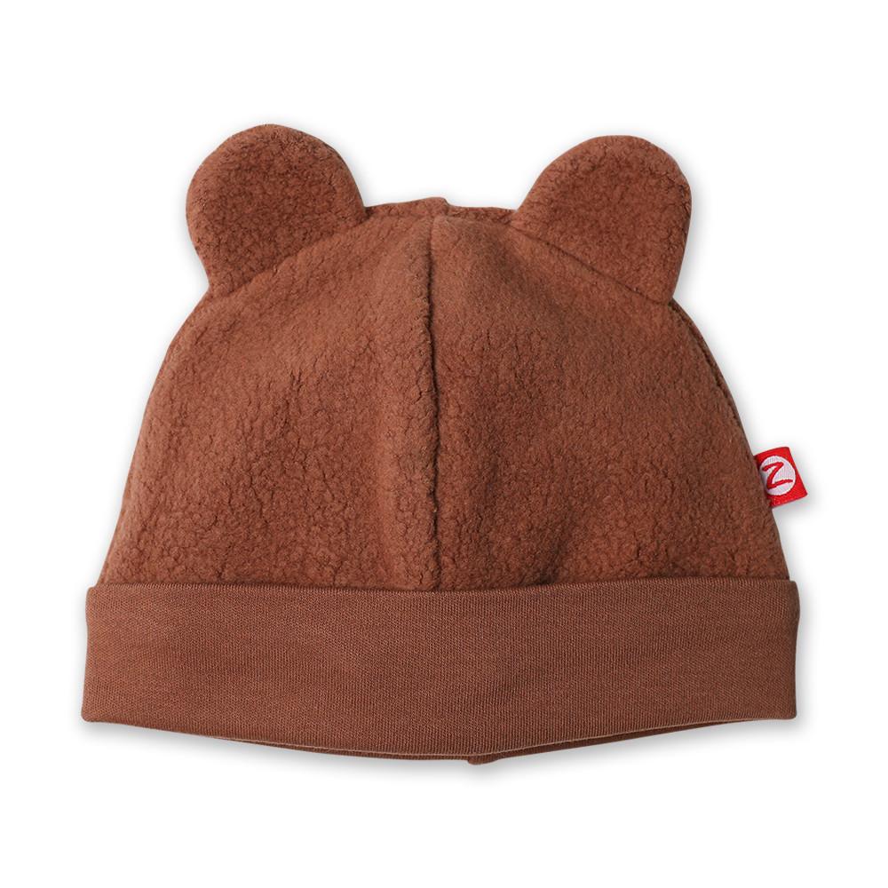 A brown fleece baby hat with ears resembling a bear's head, branded with a small red tag.