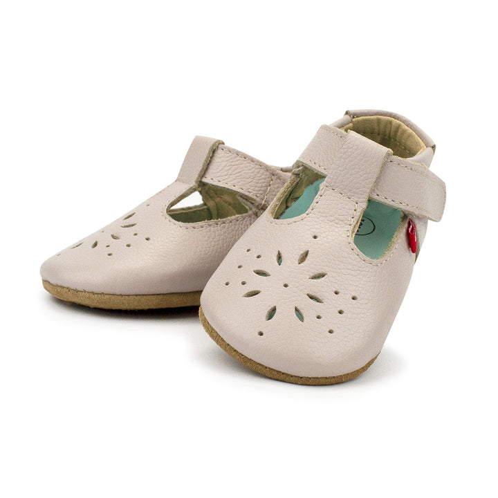 A pair of Dove colored baby Mary Jane shoes with flowery cutouts on the toes and an adjustable hook and loop strap.