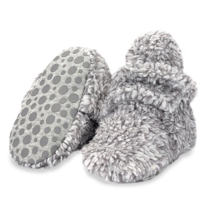 A pair of gray faux fur baby booties with gripper dots on the bottom.