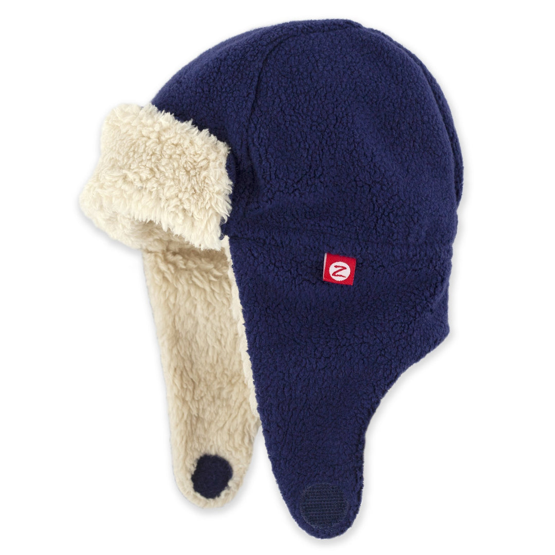 A navy blue fleece trapper hat with a beige furry lining, featuring ear flaps and a chin strap.