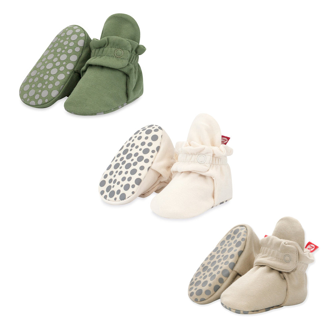 A set of organic cotton gripper baby booties in beige, khaki, and green colors with gripper patterns on the soles.