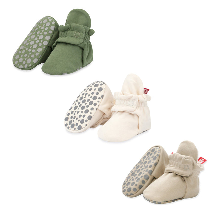A set of organic cotton gripper baby booties in beige, khaki, and green colors with gripper patterns on the soles.