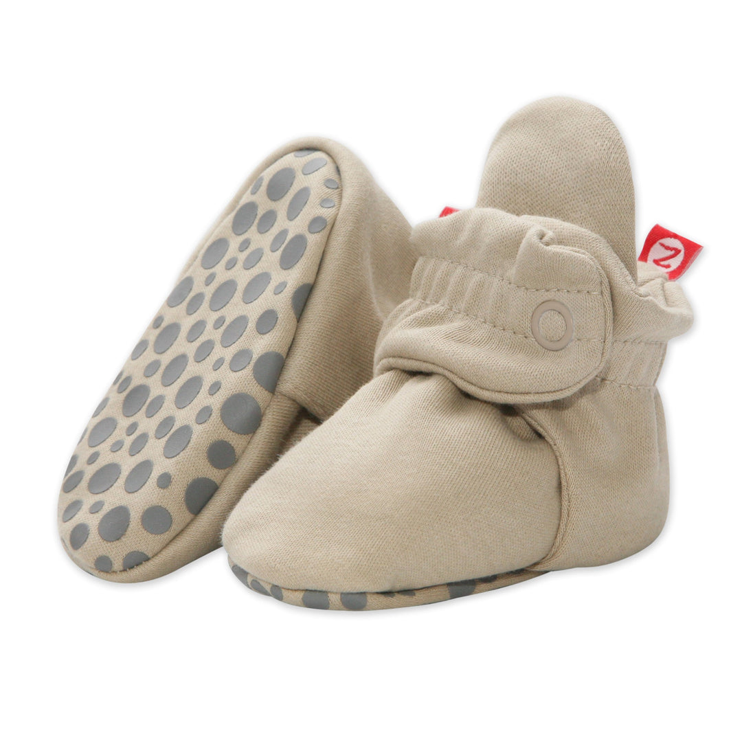 A pair of beige organic cotton baby booties with rubber grippers on the soles, displayed against a white background.
