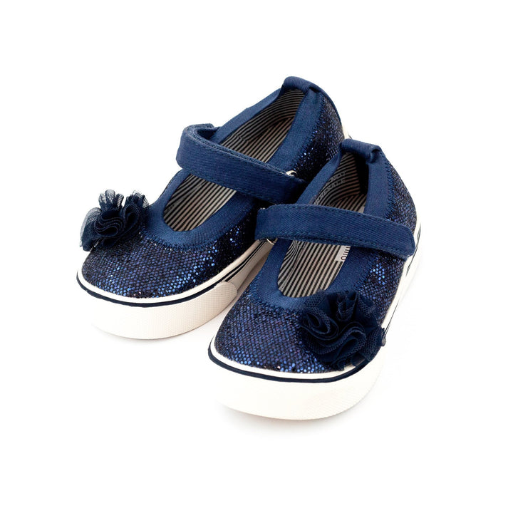 A pair of navy glittery children's Mary Jane shoes with a hook and loop strap and decorative pom-poms on the vamp.