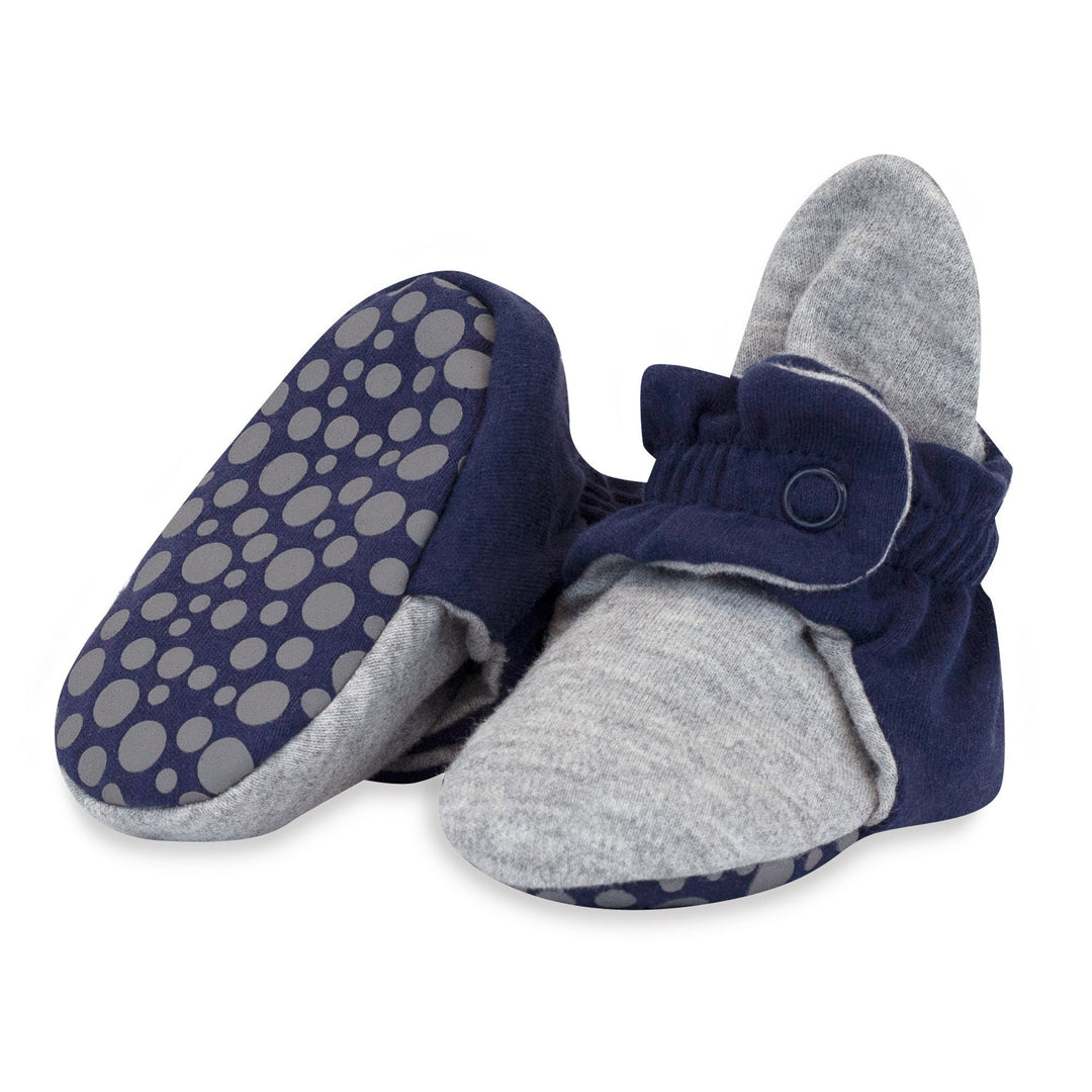 A pair of organic cotton baby booties in true navy and heather gray with rubber grippers on the soles.