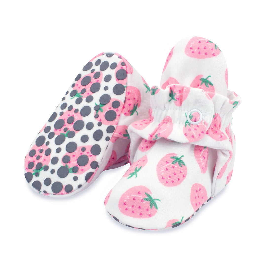 A pair of pink baby booties with a strawberries print and rubber grippers on the sole.