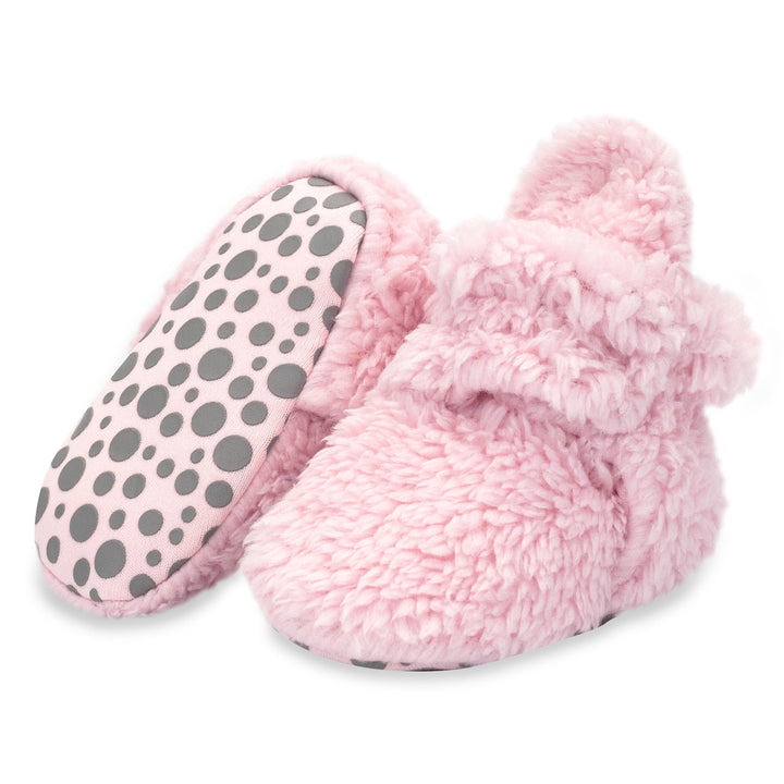 A pair of pink baby booties with faux fur exterior and gripper soles, displayed against a white background.