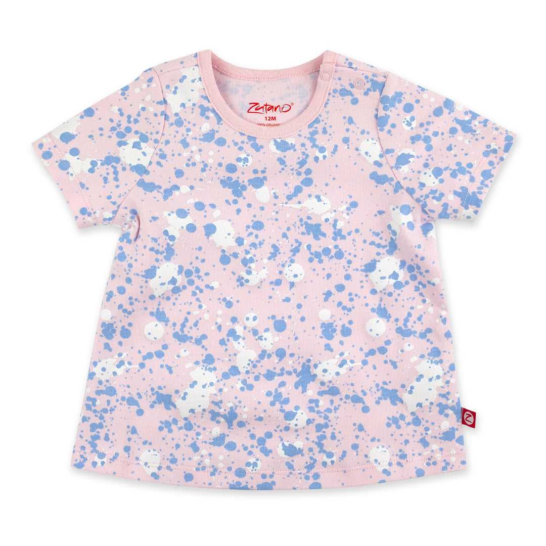 A short-sleeved baby pink t-shirt with a paint splatter print, featuring a round neckline and a small brand logo on the lower right side.