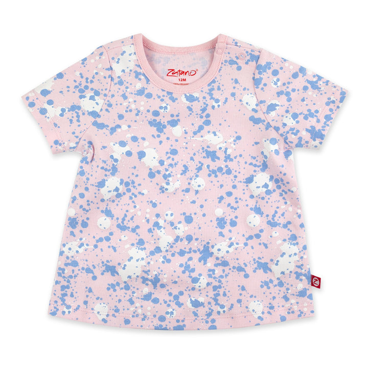 A short-sleeved baby pink t-shirt with a paint splatter print, featuring a round neckline and a small brand logo on the lower right side.