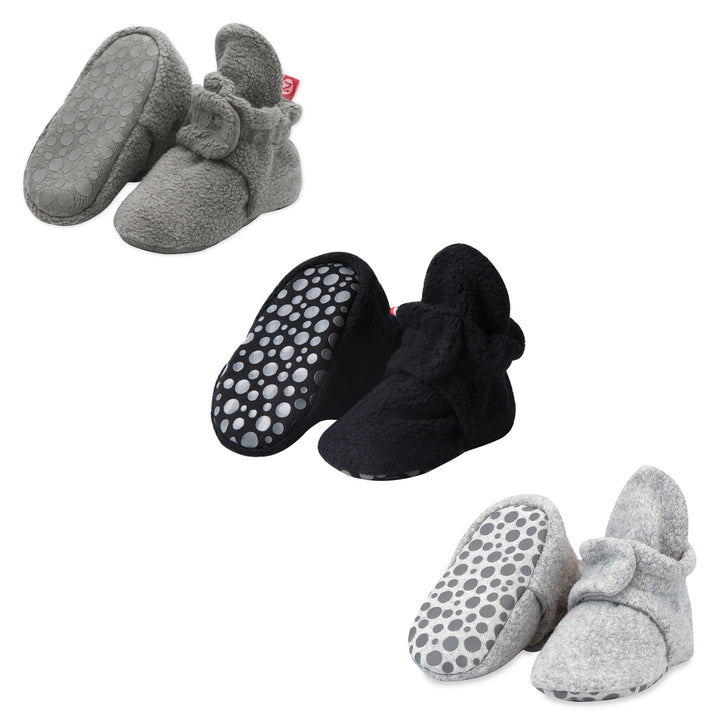 Three pairs of fleece baby booties in gray, black, and heather gray colors, displayed with gripper soles visible.