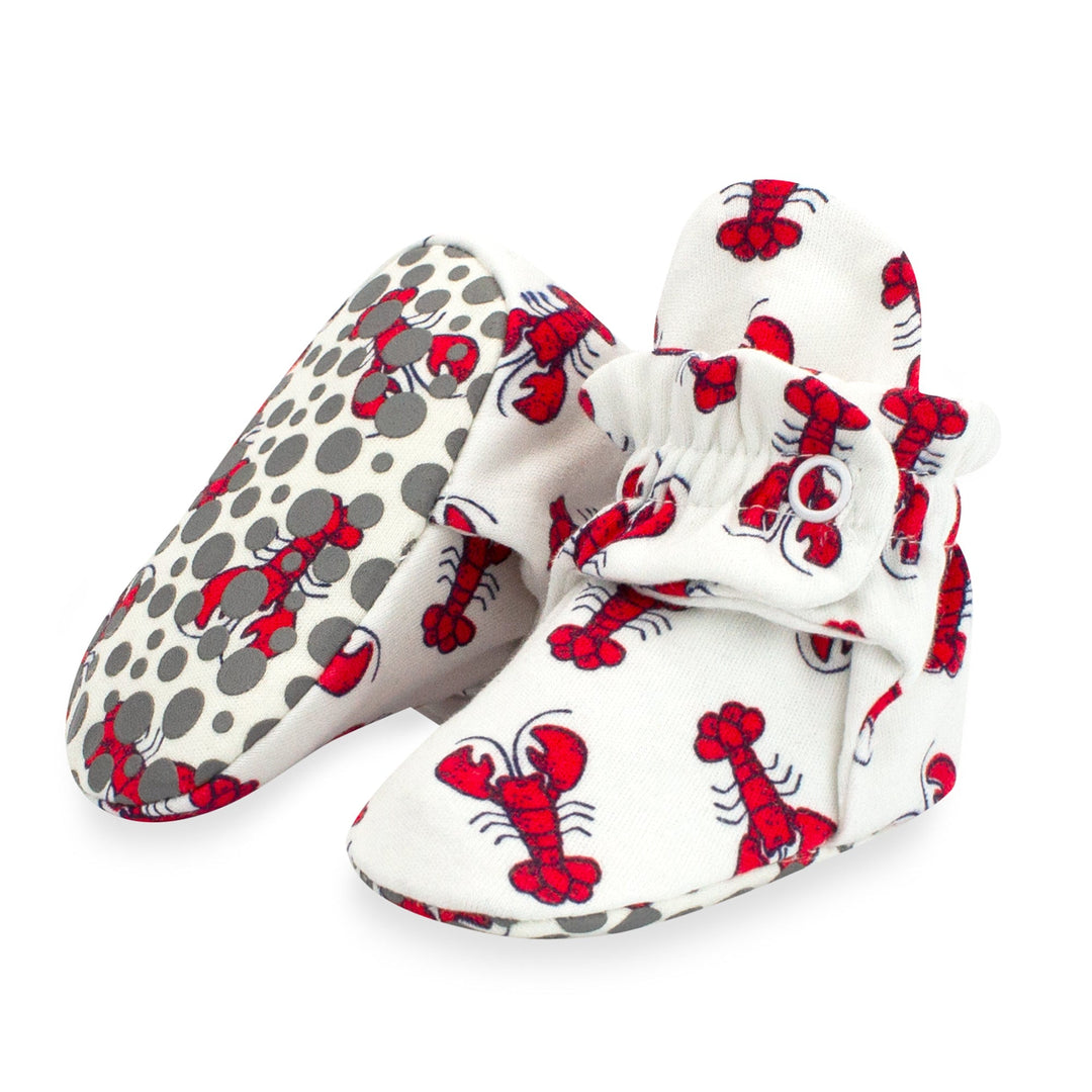 A pair of white baby booties with a red lobster print and gray dots, featuring rubber grippers on the bottom.
