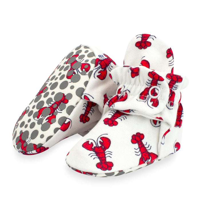 A pair of white baby booties with a red lobster print and gray dots, featuring rubber grippers on the bottom.