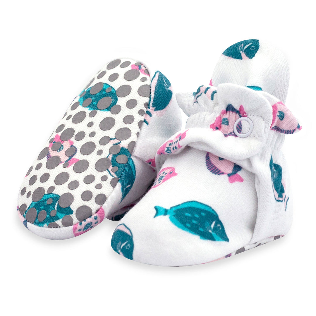 A pair of white baby booties with a tropical fish print, featuring polka dots and a two-snap secure fit design.