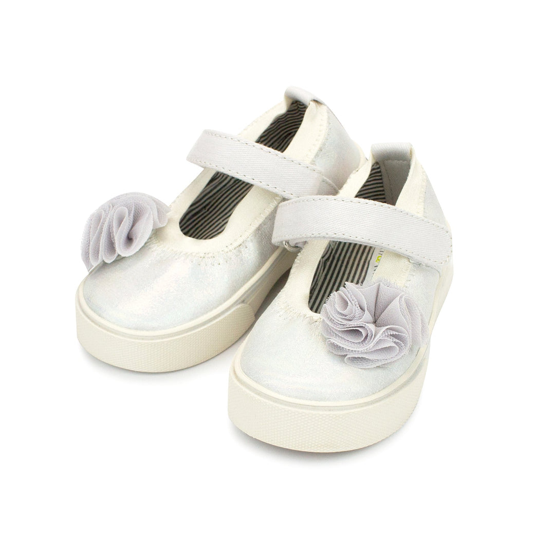 A pair of white iridescent glittery Mary Jane shoes with a hook and loop strap and decorative flower embellishments on the top.