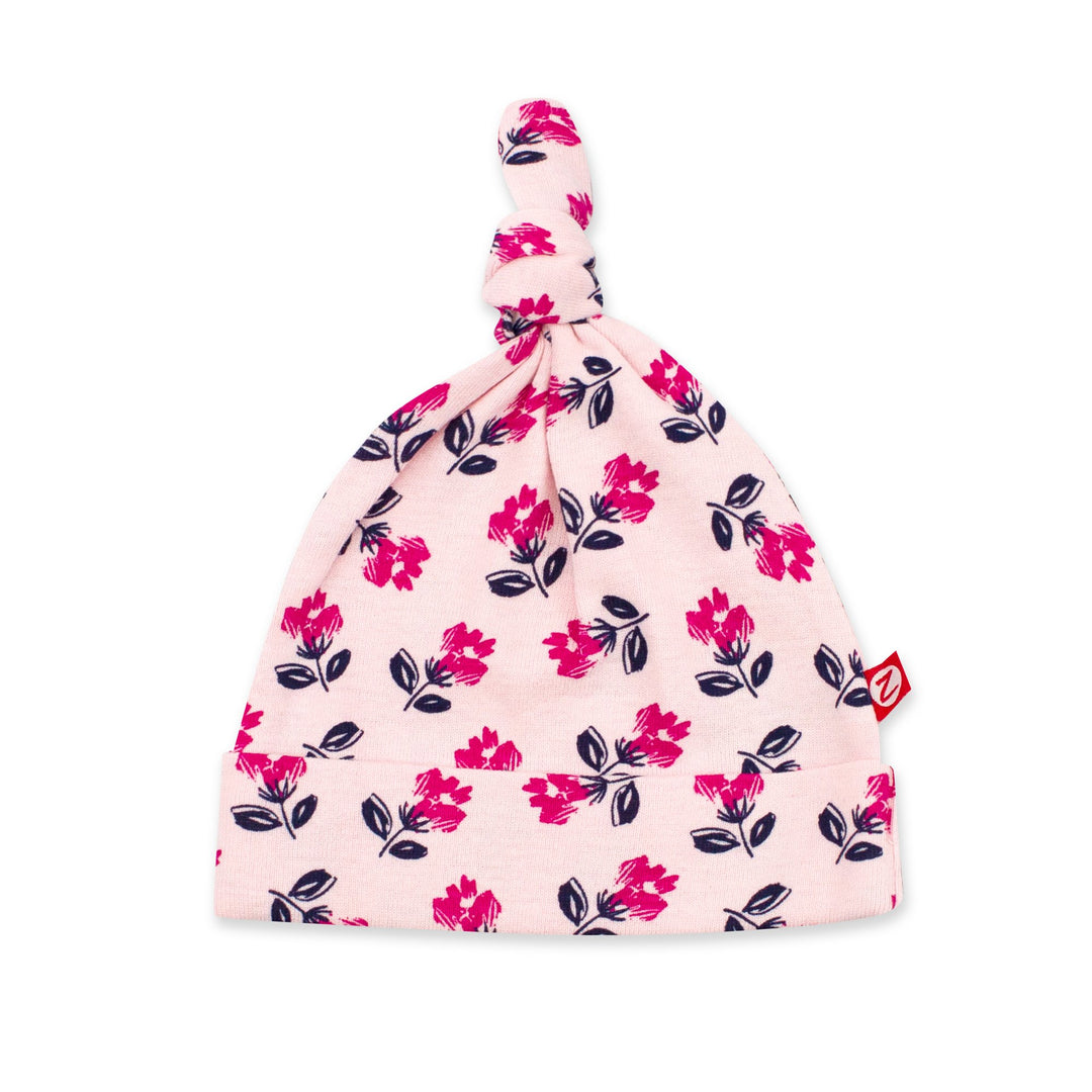 A pink organic cotton baby hat with a floral pattern, featuring a knot at the top and a folding brim.